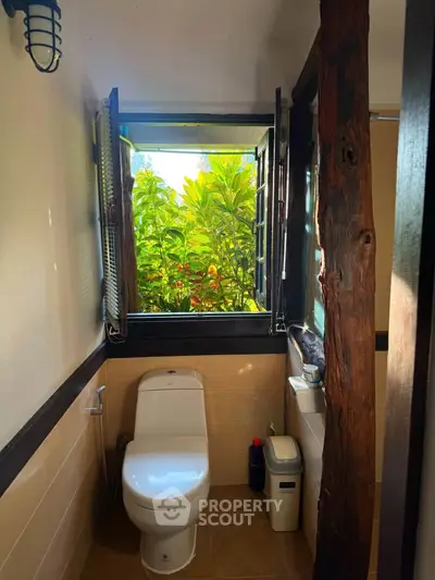 Charming bathroom with a view of lush greenery through an open window, featuring rustic wooden accents.