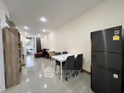 Modern open-plan living and dining area with sleek furniture and large fridge.