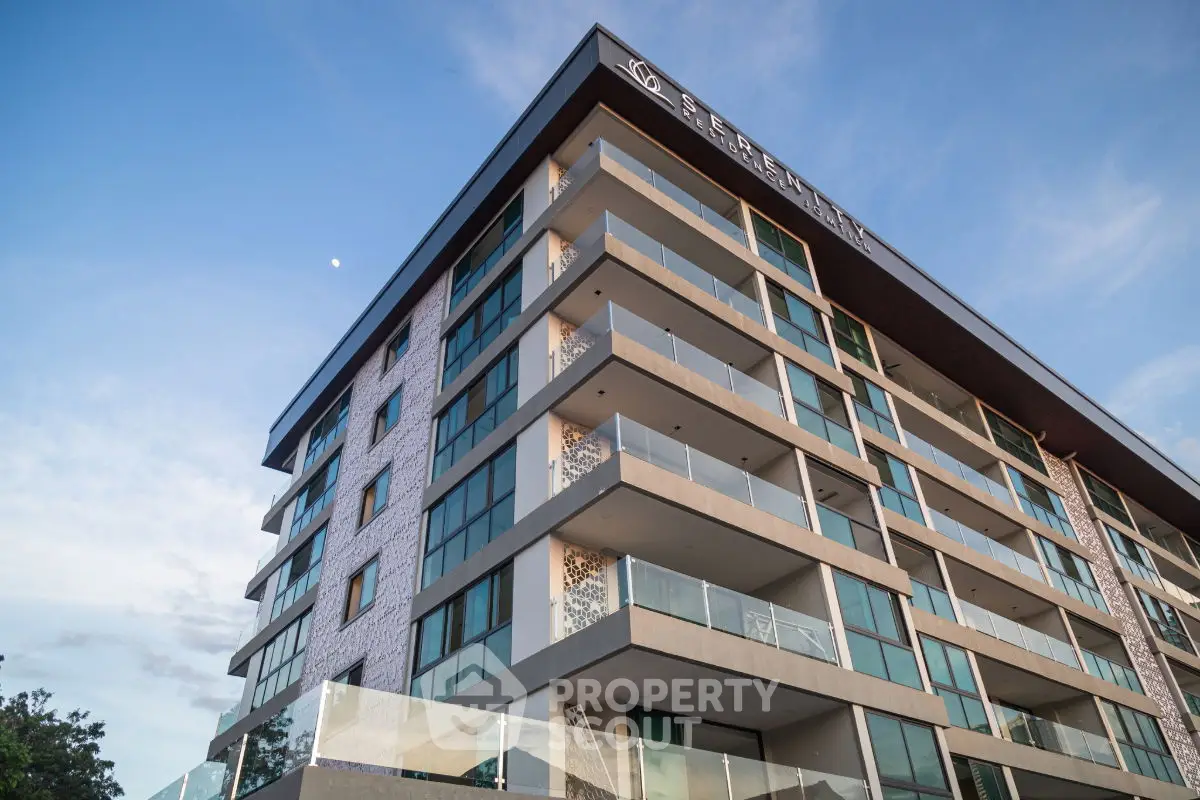 Modern multi-story residential building with spacious balconies and glass facade under a clear blue sky.