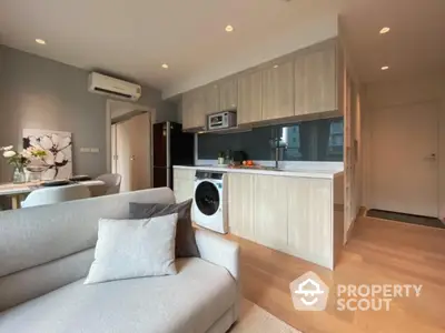 Modern open-plan living room with integrated kitchen and washing machine, featuring sleek cabinetry and cozy seating.