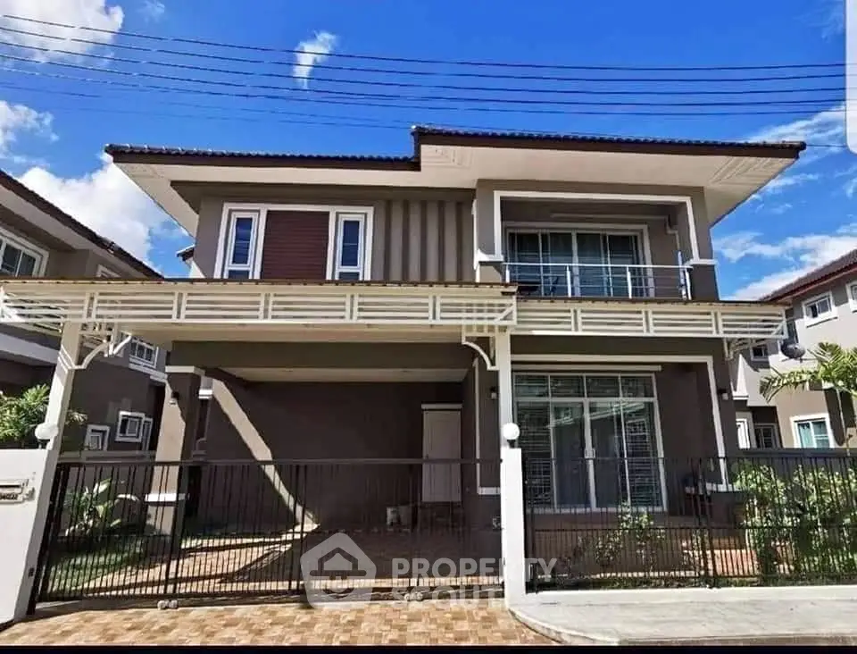 Modern two-story house with balcony and gated driveway under clear blue sky.