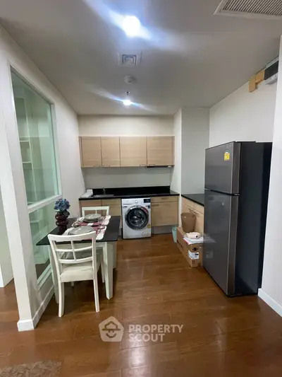 Modern kitchen with wooden flooring, sleek cabinets, and integrated washing machine in a cozy apartment.