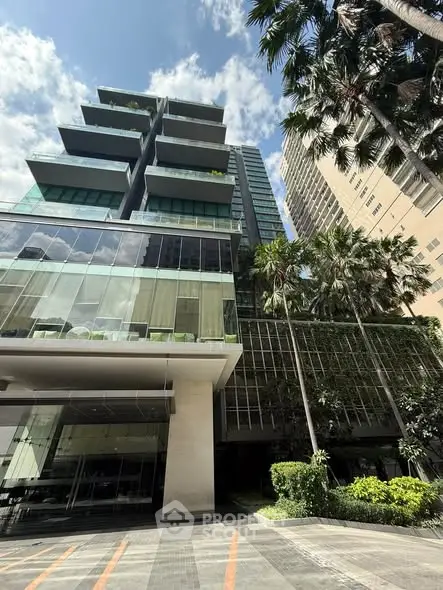Modern high-rise building with glass facade and lush greenery in urban setting.