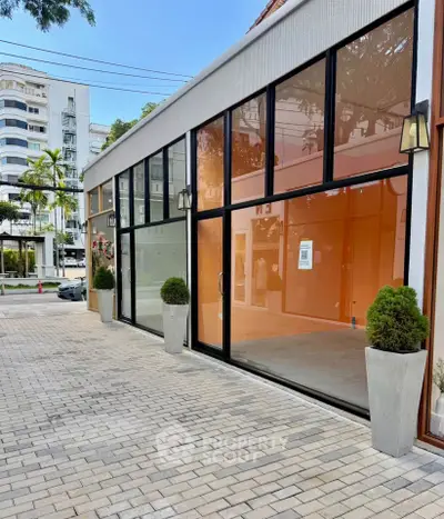 Modern commercial building exterior with large glass windows and potted plants on a paved walkway.