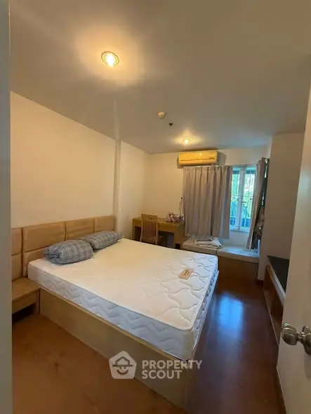 Cozy bedroom with wooden flooring, large window, and air conditioning in modern apartment.