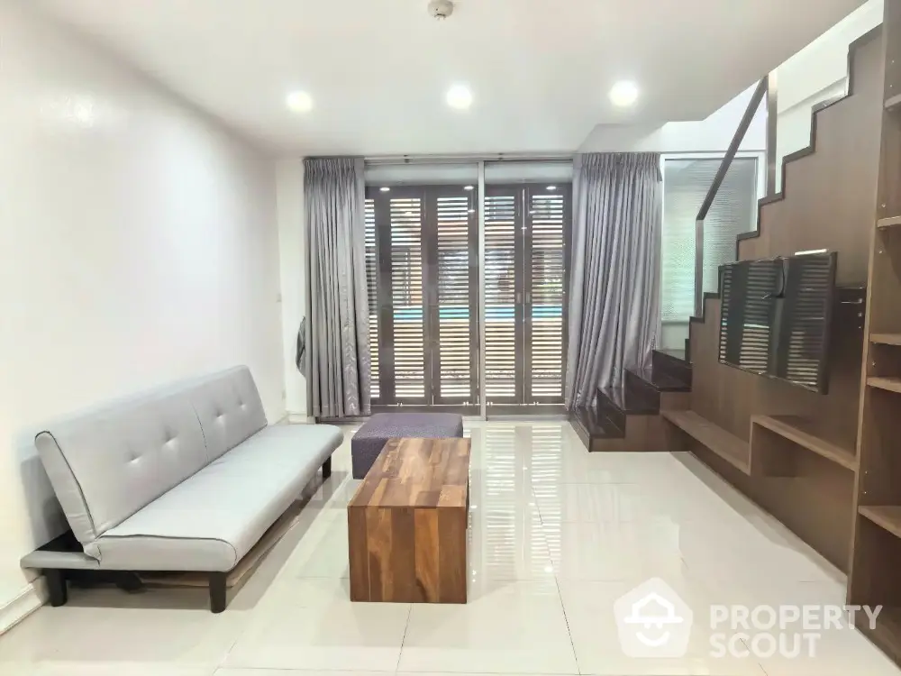 Modern living room with sleek staircase and pool view, featuring minimalist furniture and natural light.