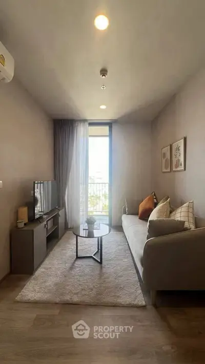 Modern living room with cozy sofa, TV, and natural light from large window.