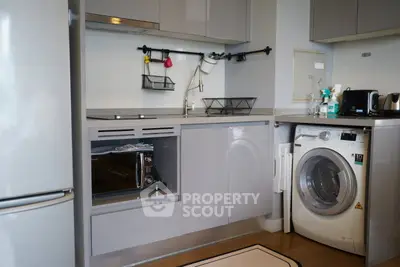 Modern kitchen with sleek cabinets, washing machine, and stainless steel fridge