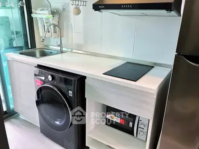 Modern compact kitchen with washing machine, microwave, and sleek appliances in a stylish apartment.