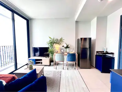 Modern living room with stylish decor and open kitchen layout, featuring a sleek fridge and cozy seating area.