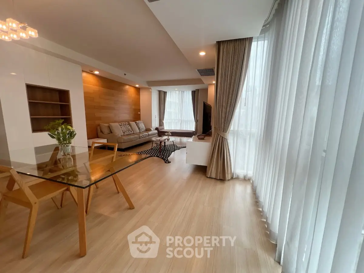 Spacious modern living room with glass dining table and cozy seating area, featuring floor-to-ceiling windows.