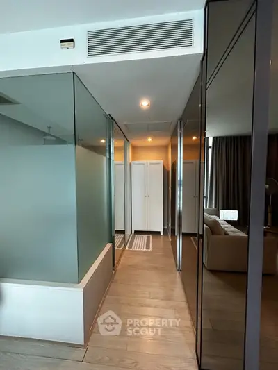 Modern apartment interior with glass partitions and wooden flooring, featuring a cozy living area and ample natural light.