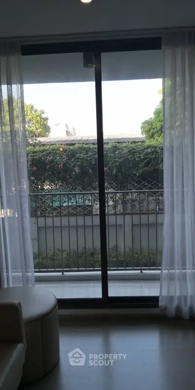 Charming balcony view with lush greenery and natural light through sliding glass doors.