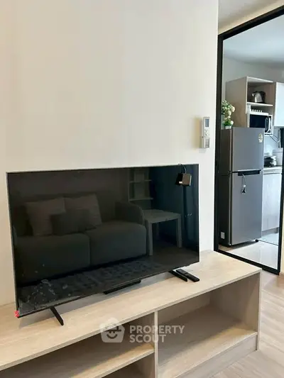 Modern living room with sleek TV and view into stylish kitchen with stainless steel fridge.