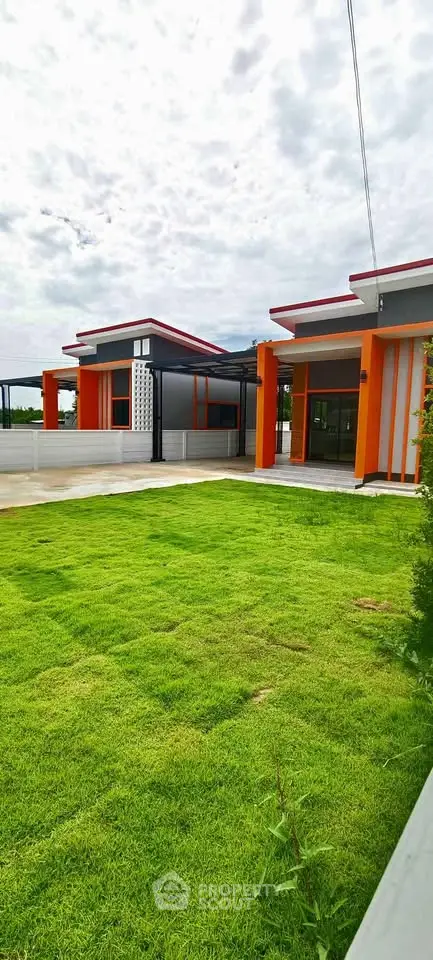 Modern single-story home with vibrant orange accents and lush green lawn, perfect for contemporary living.