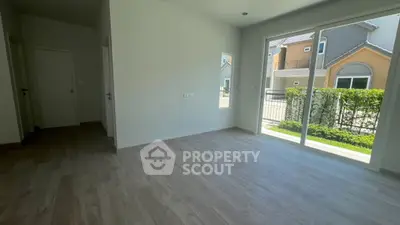 Spacious empty room with large window and view of modern houses outside.