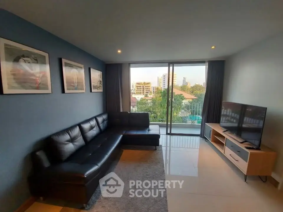 Modern living room with sleek black leather sofa and large TV, featuring a stunning city view from the balcony.