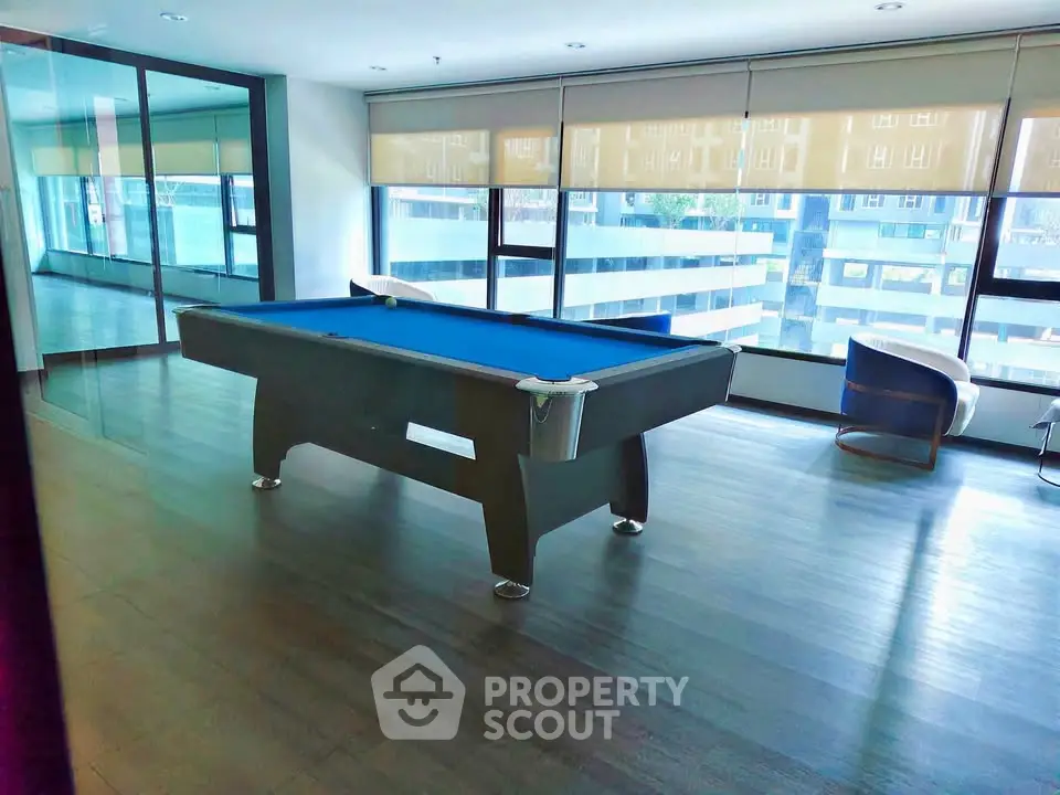 Modern apartment common area with pool table and large windows offering city views.
