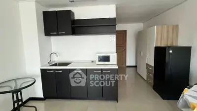 Modern compact kitchen with sleek black cabinets and appliances in a cozy apartment setting.
