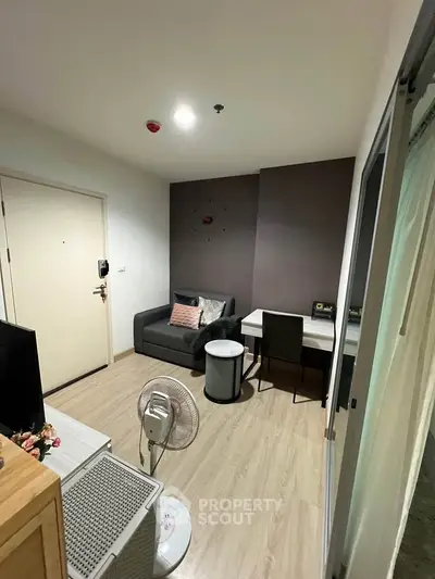 Cozy living room with modern decor and wooden flooring, featuring a sofa, desk, and fan for comfort.