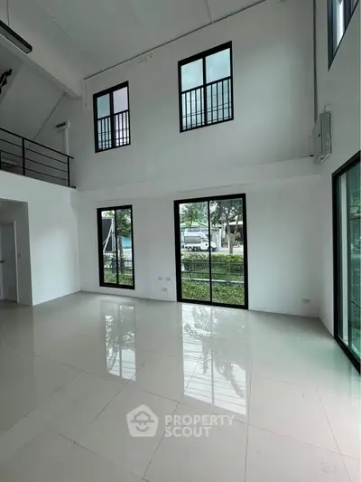 Spacious modern living room with high ceilings and large windows offering natural light and garden views.