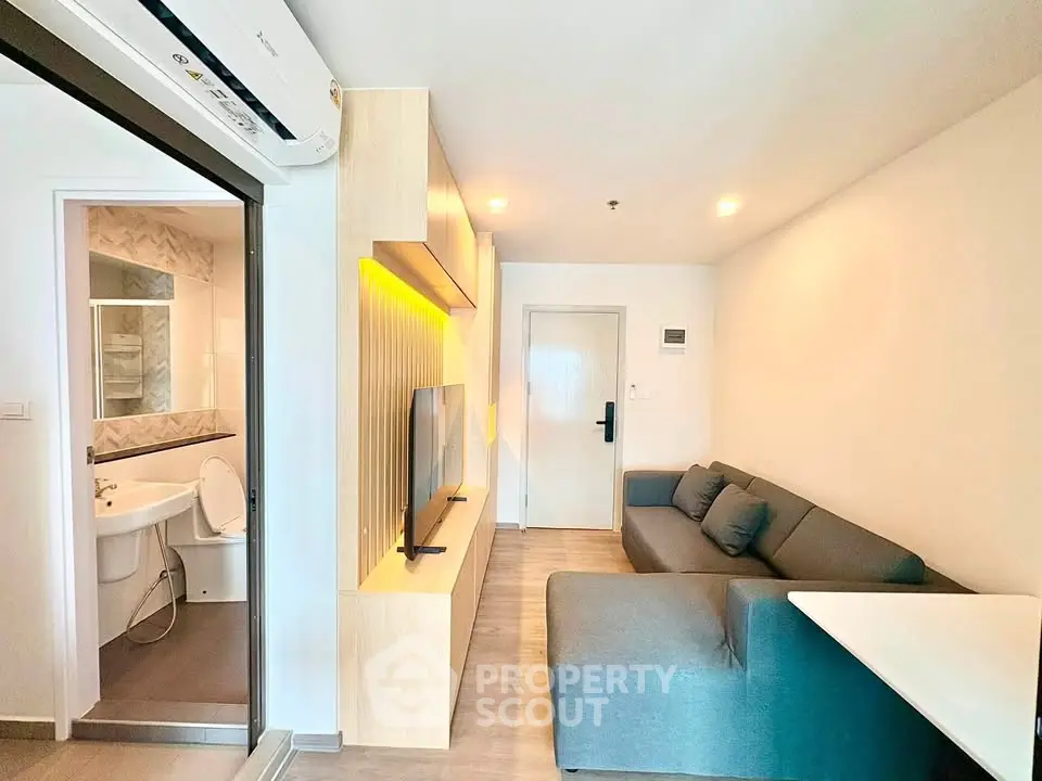 Modern living room with sleek design and integrated bathroom, featuring cozy sofa and wall-mounted TV.
