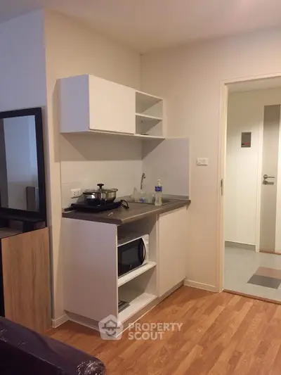 Compact kitchen with modern appliances and wooden flooring in cozy apartment.