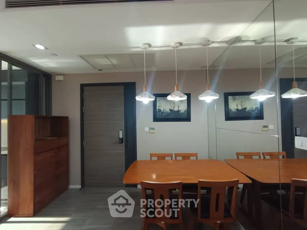 Modern dining area with wooden table and chairs, stylish pendant lights, and mirrored wall for spacious feel.