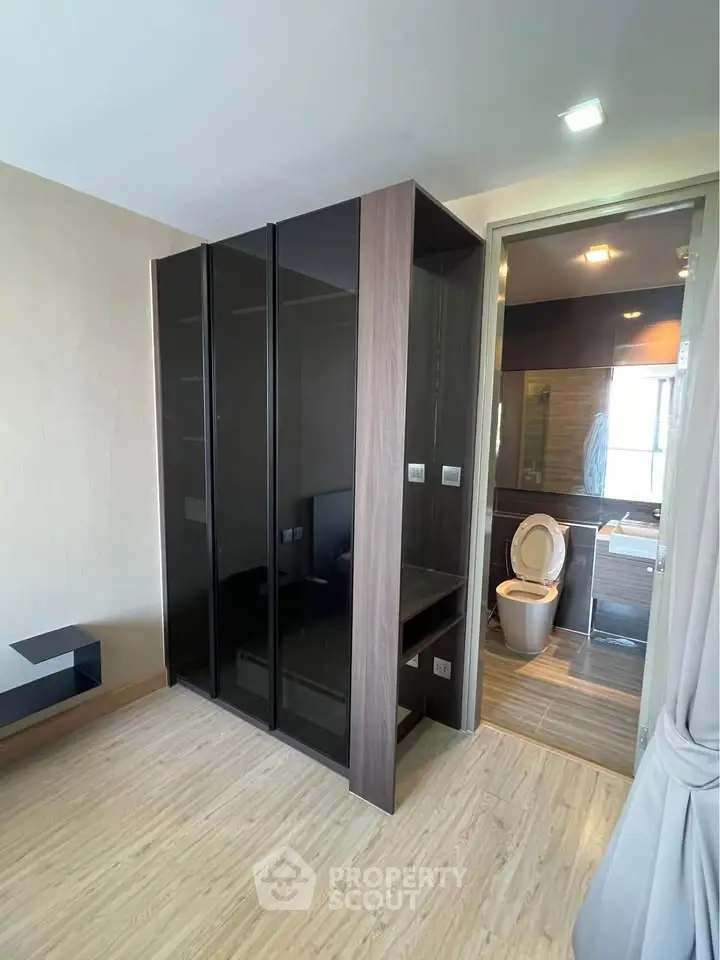 Modern bedroom with ensuite bathroom featuring sleek black wardrobe and wooden flooring.