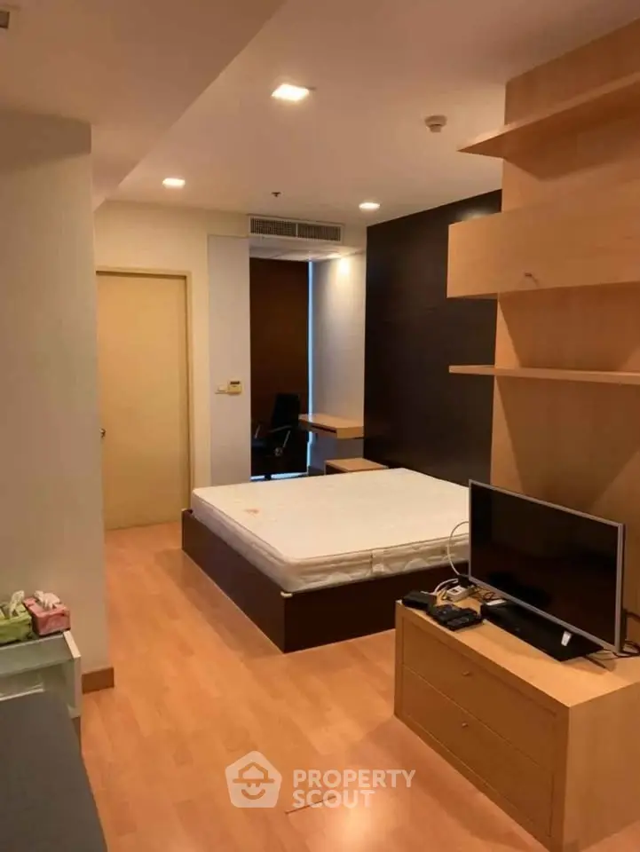 Modern bedroom with wooden flooring and built-in shelves, featuring a cozy bed and TV unit.