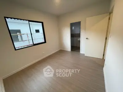Spacious empty room with wooden flooring and large window, ideal for customization.