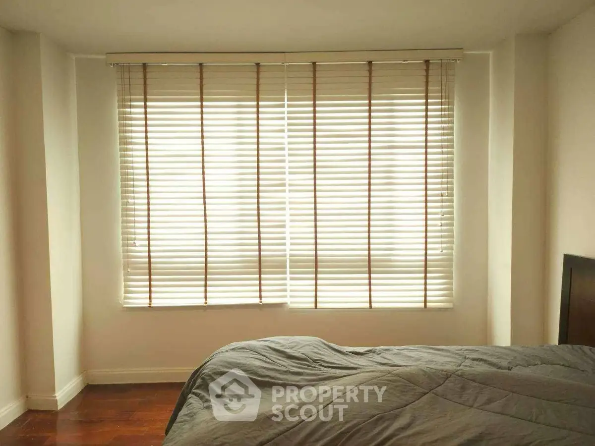 Cozy bedroom with large window and blinds, featuring a comfortable bed and warm lighting.