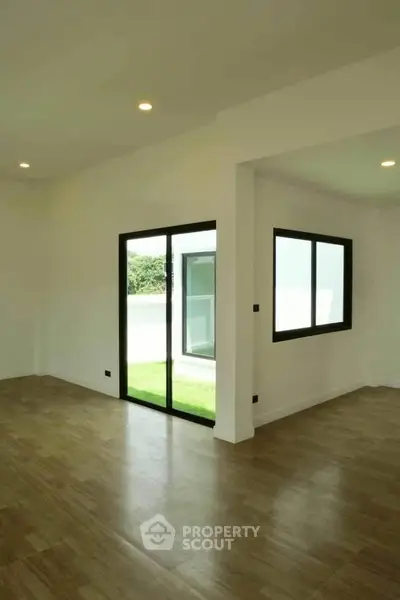 Spacious modern living room with large windows and wooden flooring, offering a bright and airy atmosphere.