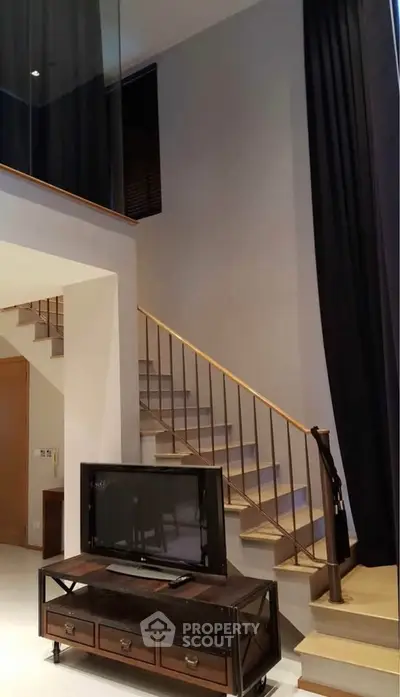 Modern living room with high ceilings and stylish staircase, featuring a sleek TV setup and elegant curtains.