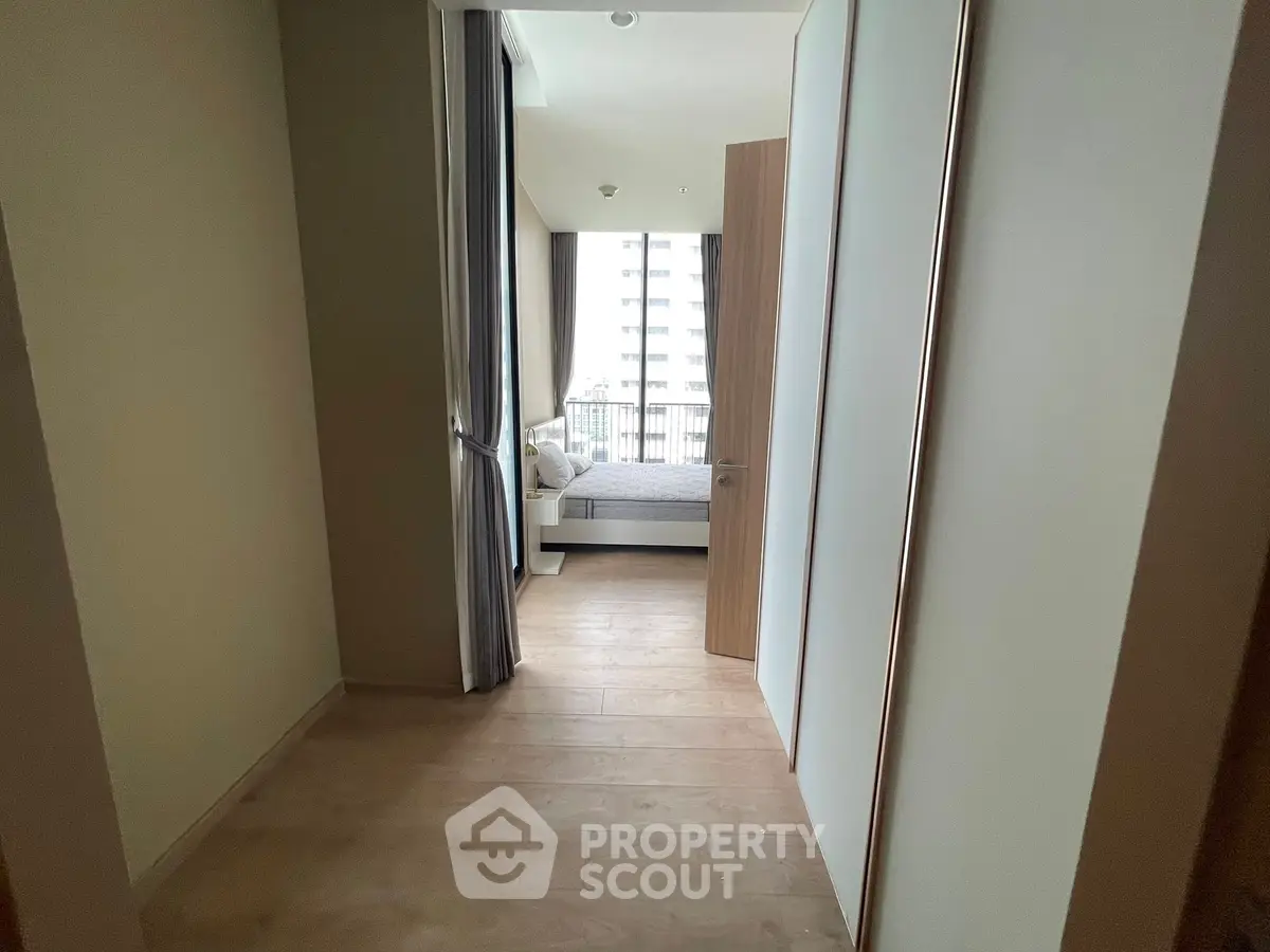 Modern apartment hallway leading to a cozy bedroom with large windows.