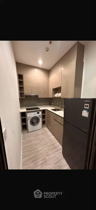 Modern kitchen with sleek cabinets, washing machine, and fridge in compact layout.
