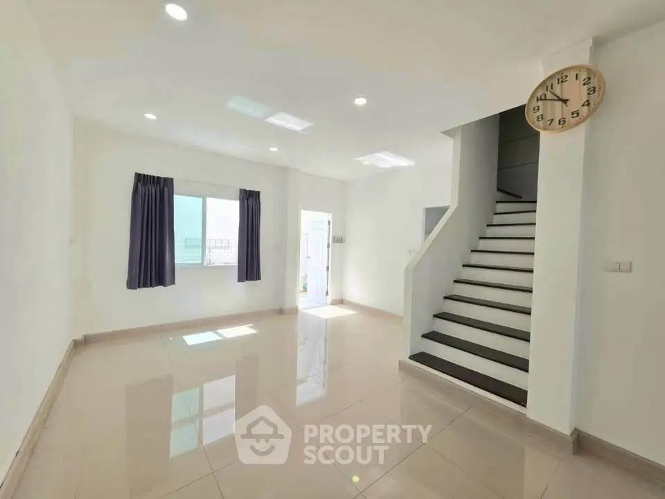 Spacious modern living room with staircase and large window, perfect for family gatherings.