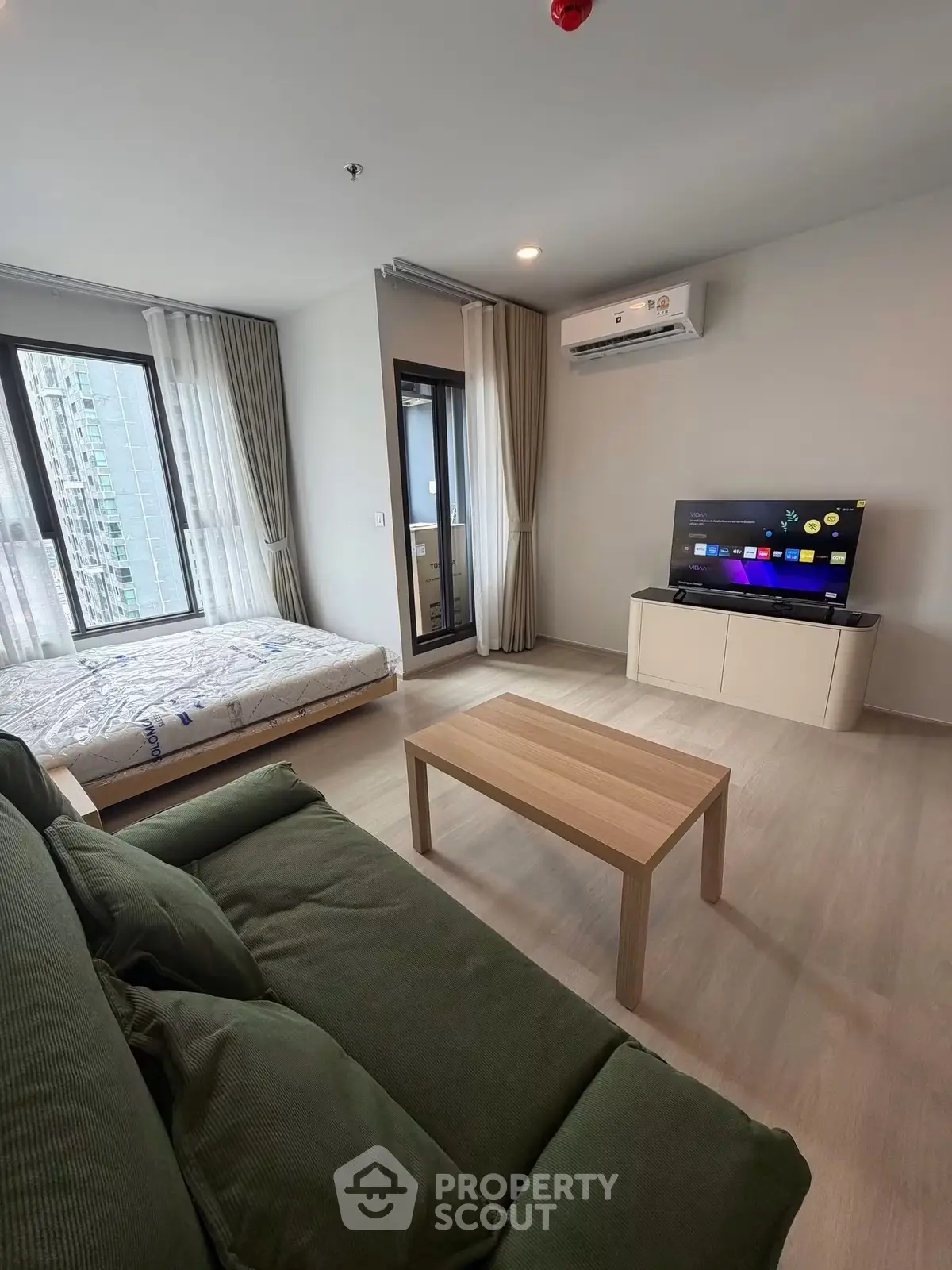 Modern studio apartment with cozy living area and large windows offering city views.