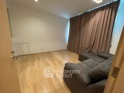 Spacious living room with wooden flooring and cozy sofa, ideal for relaxation.