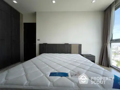 Modern bedroom with large window and city view, featuring a spacious bed and sleek wardrobe.