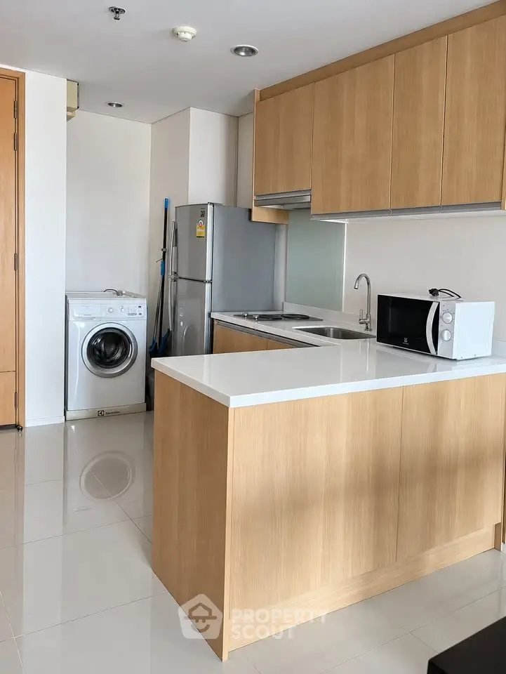 Modern kitchen with sleek wooden cabinets, washing machine, and stainless steel appliances in a bright apartment.