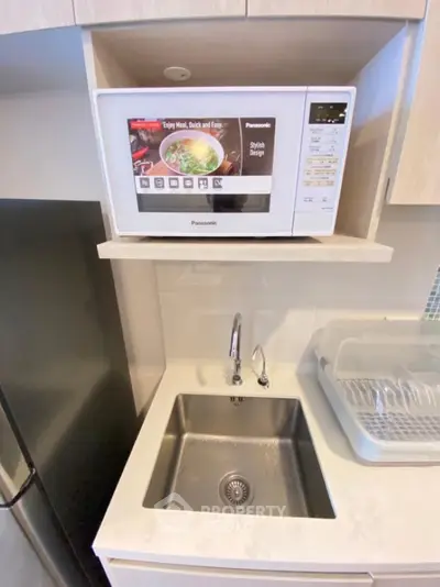 Modern kitchen with microwave and stainless steel sink, compact and efficient design.