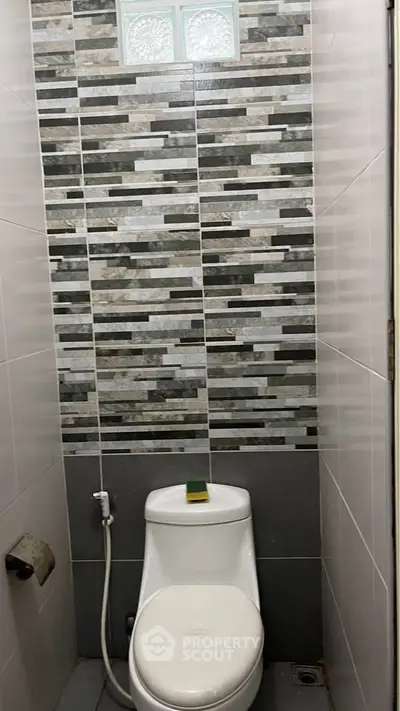 Compact bathroom with modern tiled walls and toilet, ideal for small spaces.