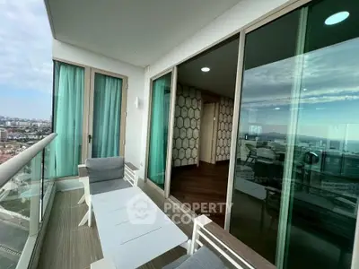 Modern apartment balcony with stunning city and ocean views, featuring sleek furniture and glass doors.