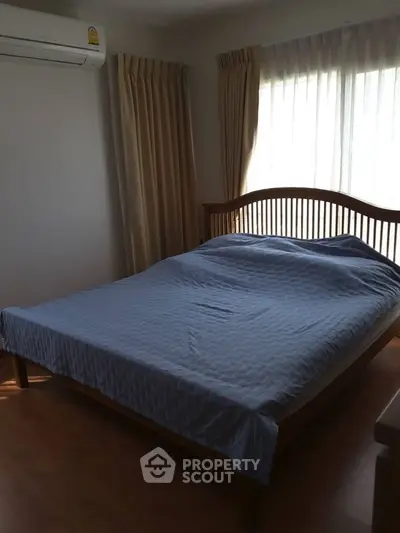 Cozy bedroom with wooden bed frame and natural light from large window.