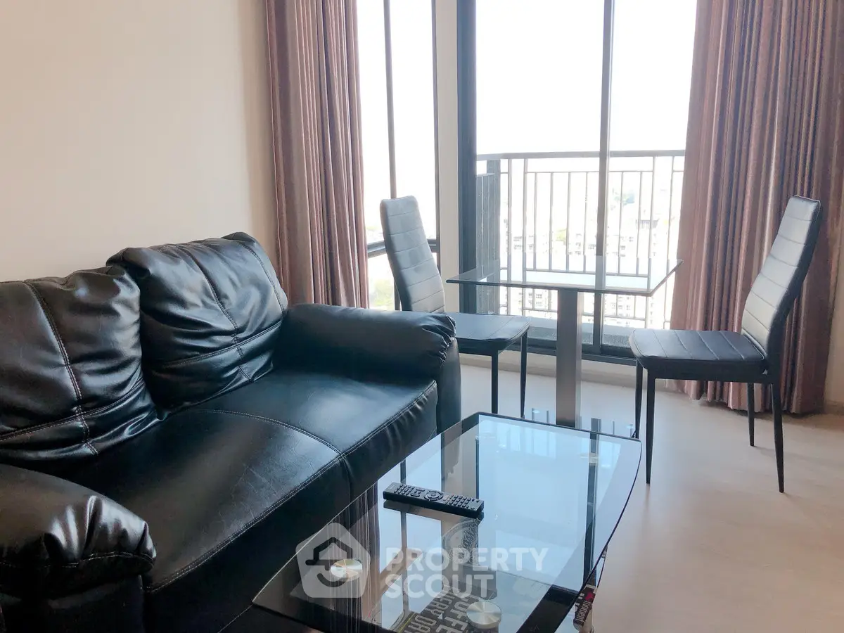 Modern living room with leather sofa and glass table, featuring a balcony view.