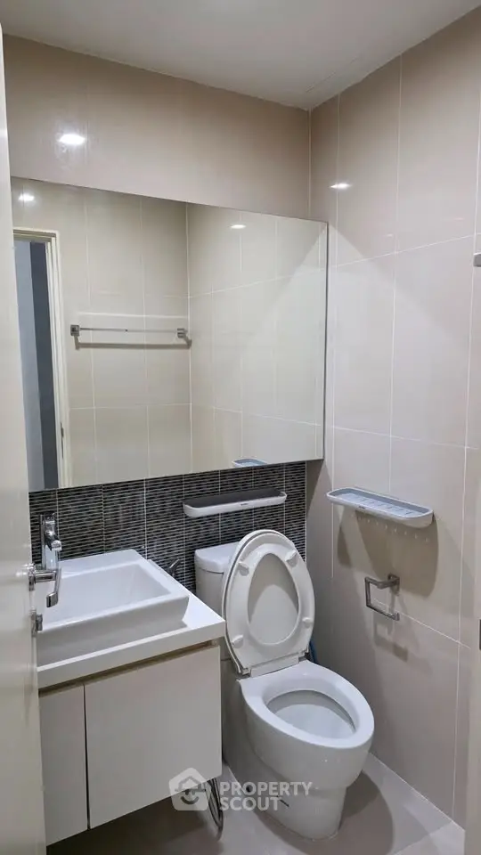 Modern bathroom with sleek fixtures and neutral tiles, featuring a compact vanity and toilet.