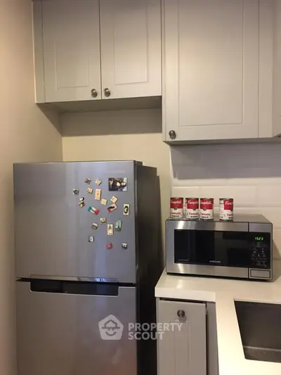 Modern kitchen with stainless steel fridge and microwave, sleek cabinetry, and minimalist design.