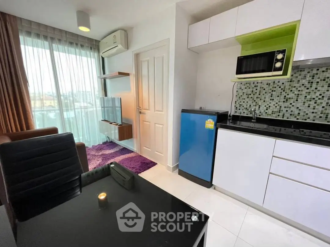 Modern studio apartment with compact kitchen and cozy living area, featuring a vibrant purple rug and natural light.
