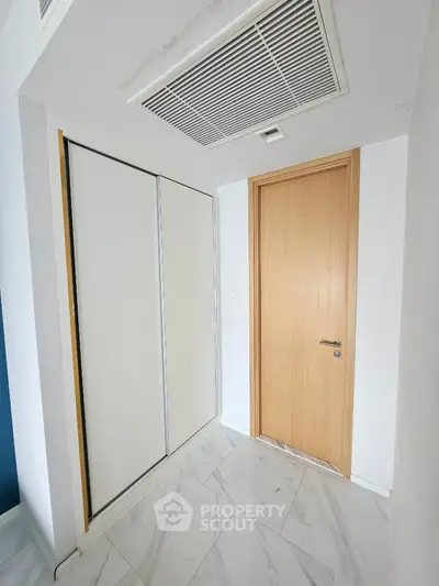 Modern hallway with wooden door and sliding closet, featuring sleek white tiles.